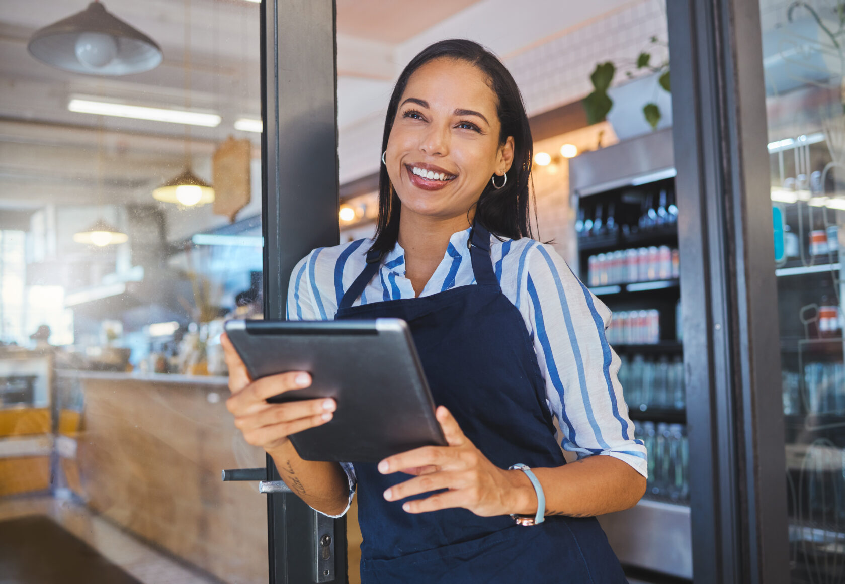 Startup, cafe and business woman in management with smile working on a digital tablet at the store Manager, coffee shop owner or worker of a small business at work in retail with technology